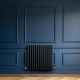 Traditional anthracite grey 4 column radiator mounted on a deep blue wall, showcasing a sleek, vintage design with polished valves