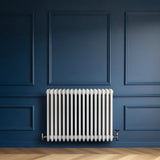 Traditional white 4 column radiator with valves, featuring a sleek design against a deep blue wall and herringbone wood floor