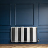 Traditional white 4 column radiator with smooth, glossy finish, mounted against a deep blue wall, enhancing modern decor