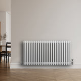 Traditional white 4 column radiator with a sleek finish, mounted on a wall in a modern room with wooden flooring and minimalist decor