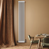 Tall, sleek white traditional 4 column radiator with black valves, mounted on a warm-toned wall beside a stylish dining area