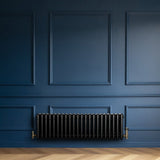 Traditional black 4 column radiator against a deep blue wall, featuring a sleek, glossy finish and vintage brass fittings