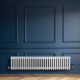 Traditional white 4 column radiator against a deep blue wall, featuring a sleek, smooth finish and classic design elements