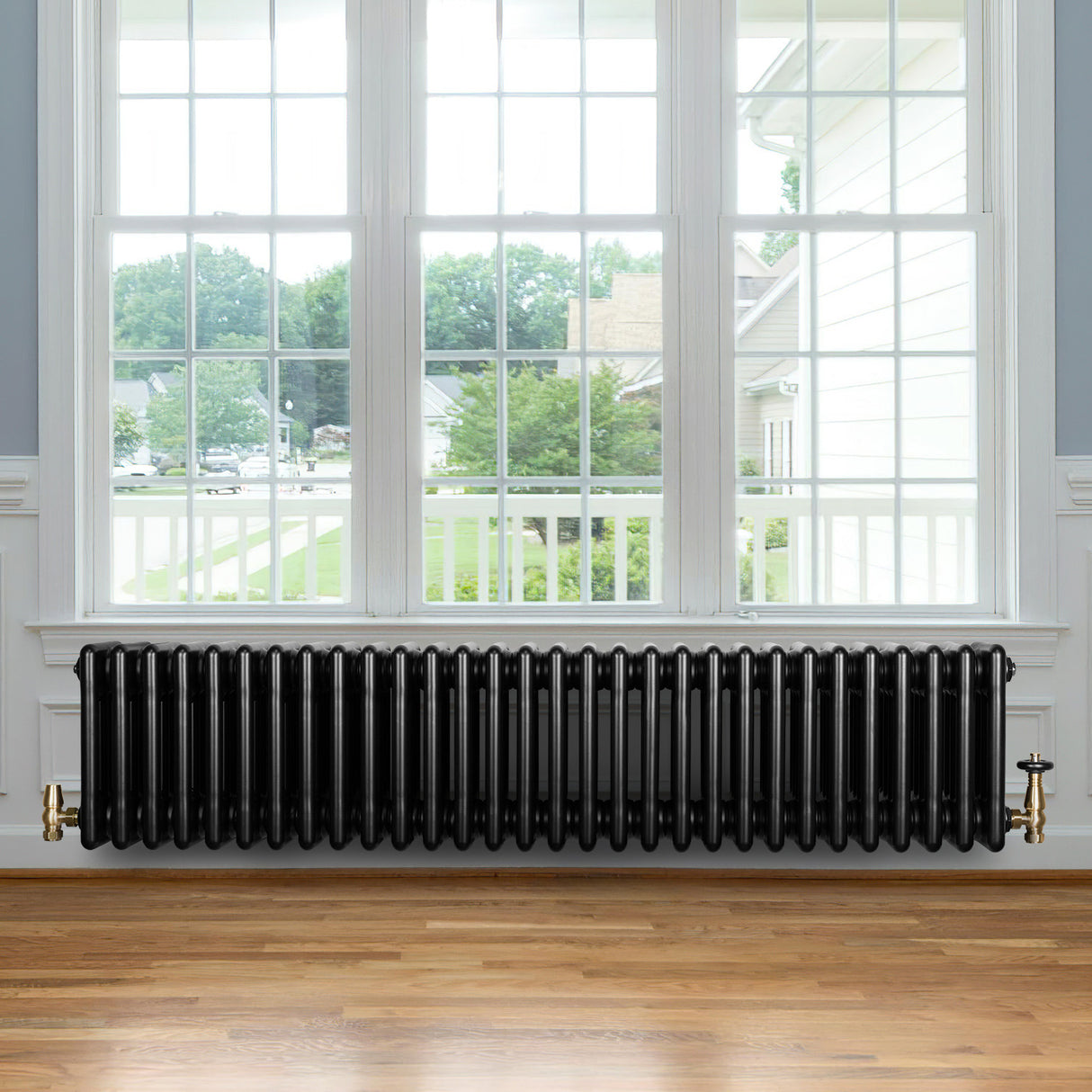 Traditional black 4 column radiator with a sleek, glossy finish, positioned beneath a large window in a bright room with wooden flooring