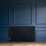 Traditional anthracite grey 4 column radiator against a deep blue wall, featuring smooth, rounded edges and a sleek finish