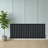 Sleek black flat single column radiator with vertical slats, positioned against a light wall, beside a potted plant on wooden flooring