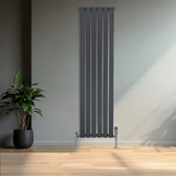 Sleek anthracite grey flat single column radiator with vertical slats, mounted on chrome feet, beside a potted plant in a modern room