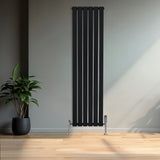 Sleek black flat single column radiator stands tall against a light wall, complemented by chrome valves and a potted plant nearby