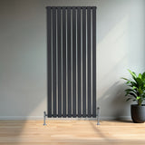 Flat single column radiator in anthracite grey, featuring vertical slats and sleek chrome feet, set against a modern interior with a plant