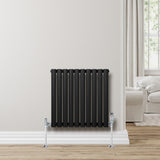Sleek black oval single column radiator, 600 x 600mm, mounted on a light wall, complemented by chrome valves and a warm wood floor