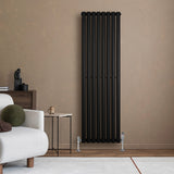 Sleek black oval single column radiator mounted on a textured beige wall, complementing a modern living room setting with a cozy sofa