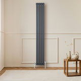 Sleek anthracite grey oval single column radiator, 1800 x 240mm, mounted on a wall with stylish wooden furniture nearby