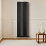 Sleek black oval single column radiator, 1800 x 600mm, mounted on a light wall, complementing a wooden table and decor elements