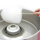 Fluffy white cotton candy being spun on a silver cotton candy machine, with a hand holding a wooden stick for serving
