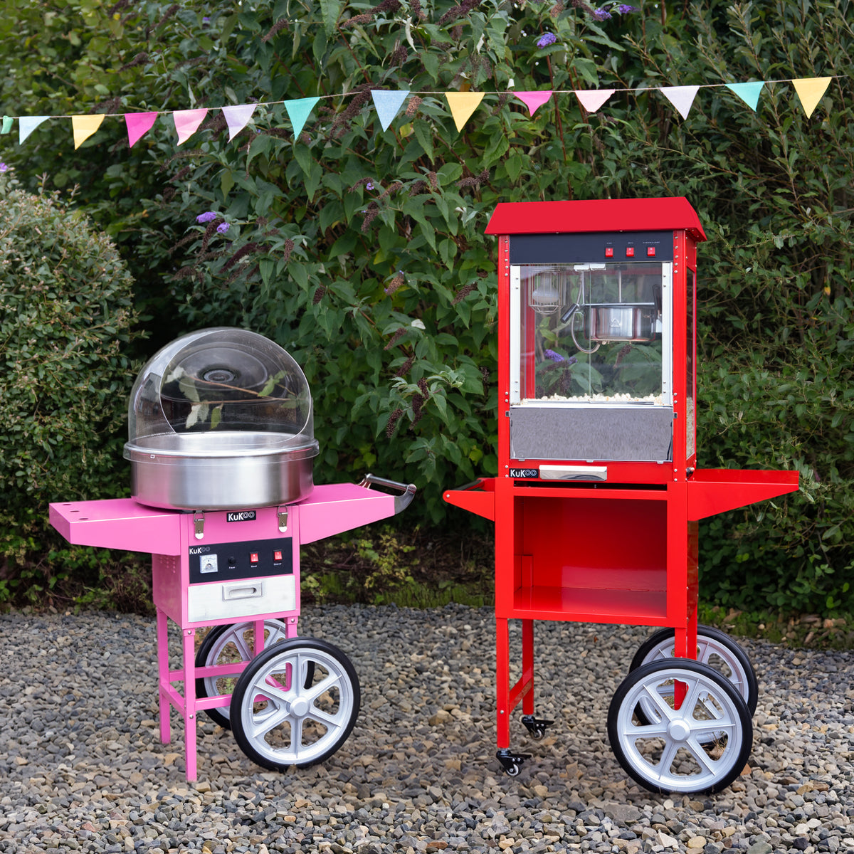 Bright pink cotton candy machine and red popcorn cart on wheels, set against a green garden backdrop with colorful bunting