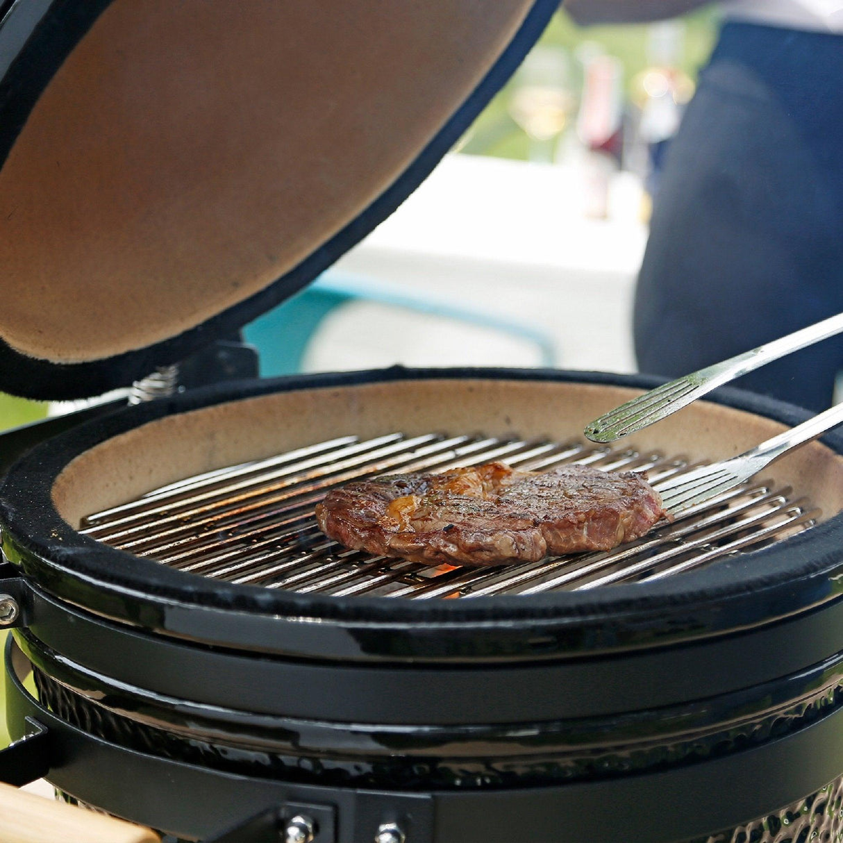 Kamado charcoal BBQ grill with a glossy black finish, featuring a ceramic interior and a juicy steak sizzling on the grill grates