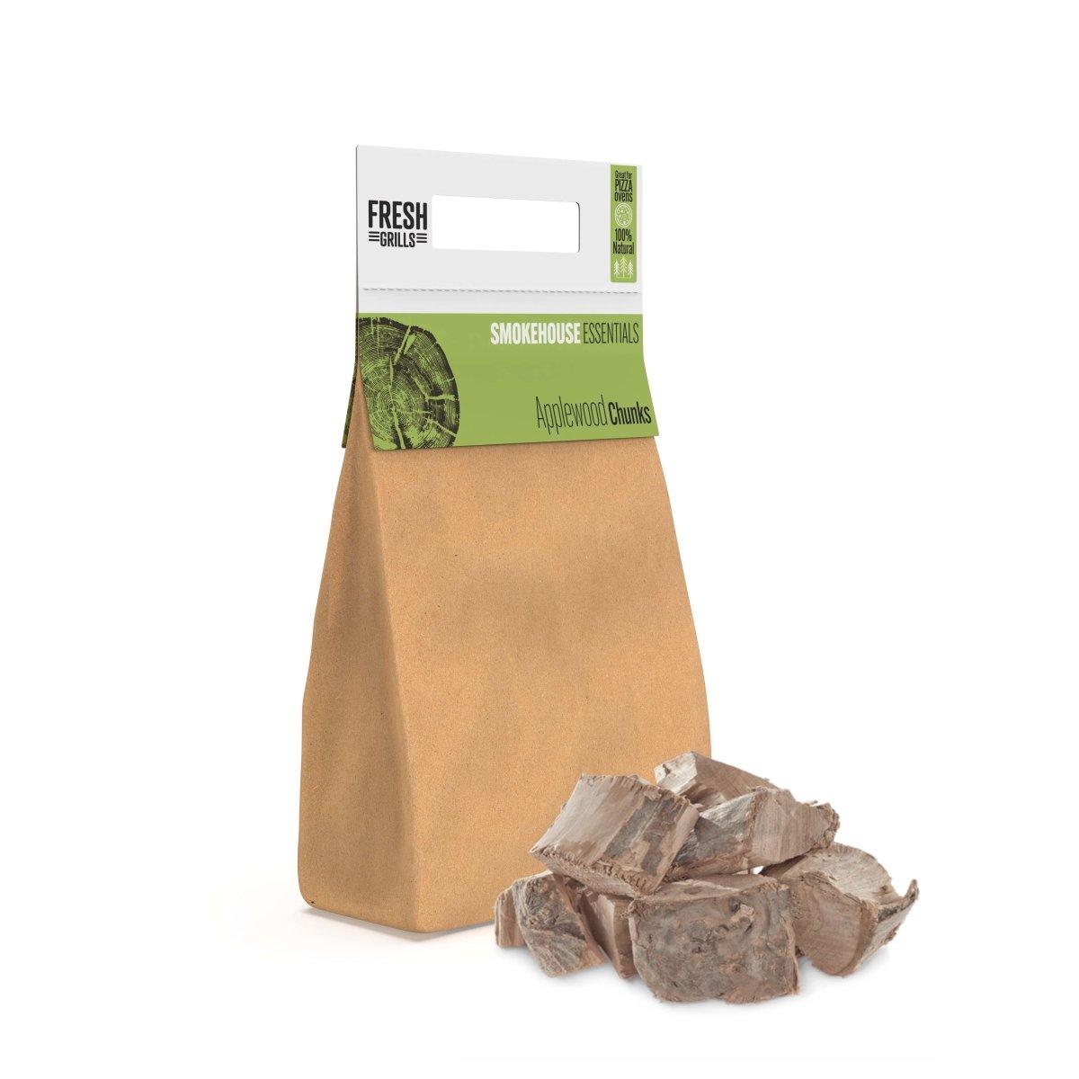 Brown paper bag filled with applewood chunks for BBQ grilling, featuring a green label and scattered wood pieces on a white background