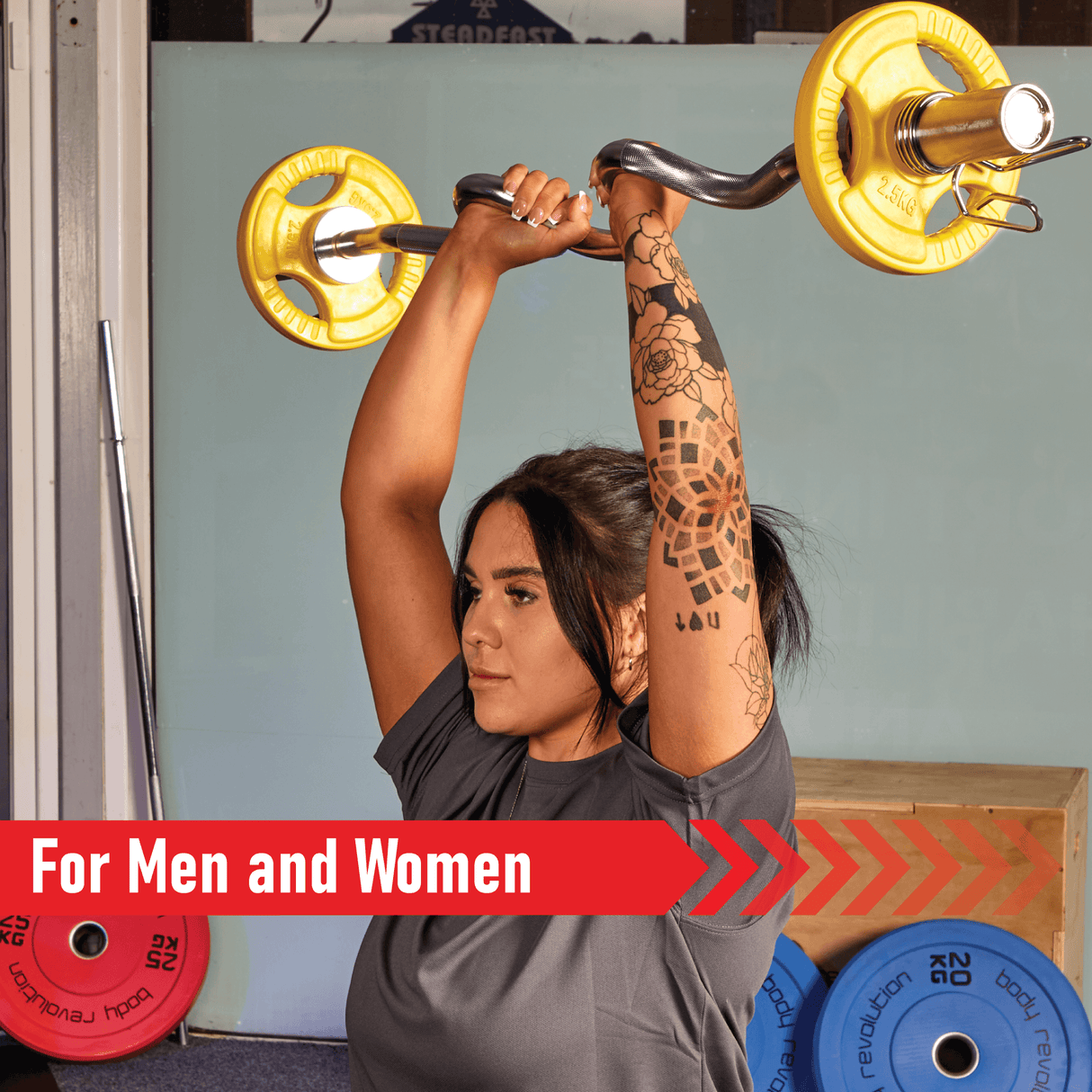 A person with a tattoo lifts a barbell with yellow Olympic tri-grip rubber weight plates in a gym setting, showcasing strength and fitness