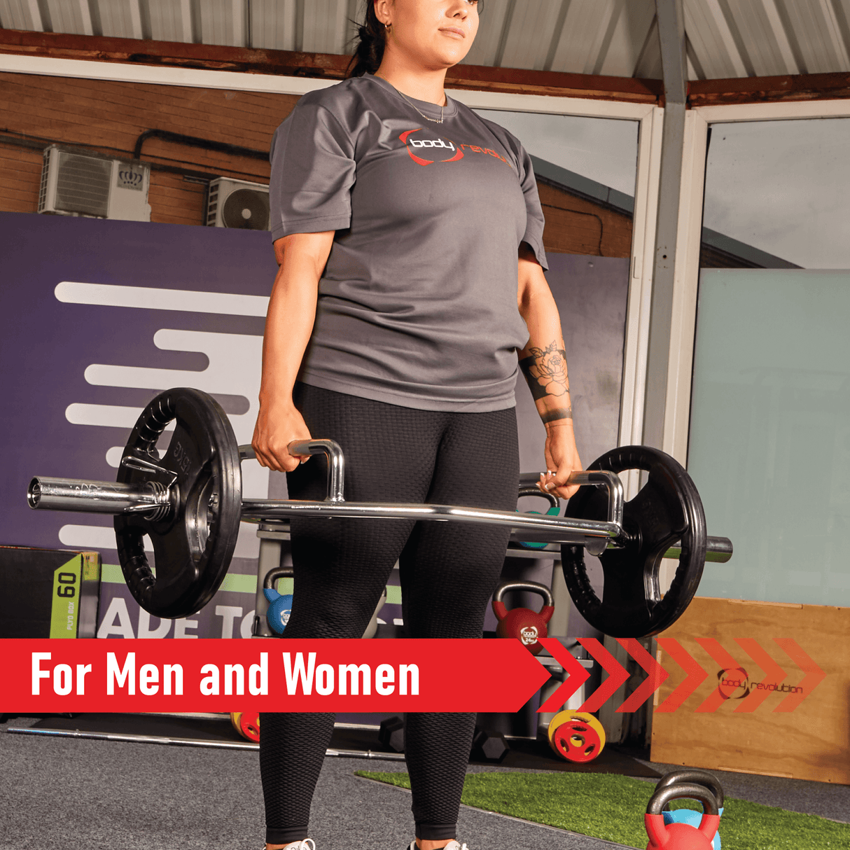 A person in a gray shirt and black leggings lifts a barbell with Olympic tri-grip rubber weight plates in a gym setting