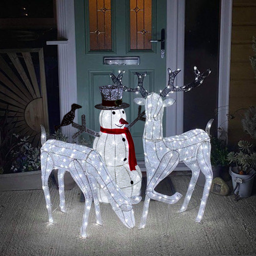 Illuminated reindeer stag, doe, and snowman with a top hat, adorned with white lights, standing on a porch by a green door
